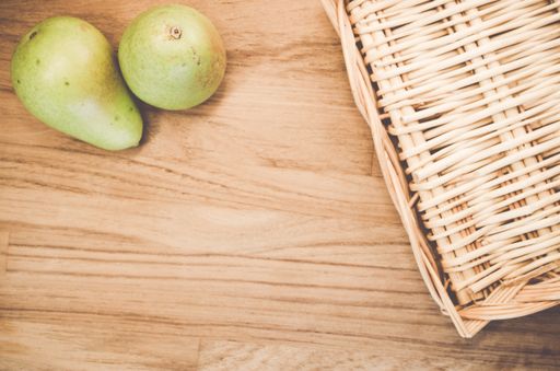 A top view of green pears on a wicker basket and wooden surface