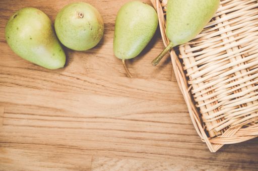 A top view of green pears on a wicker basket and wooden surface