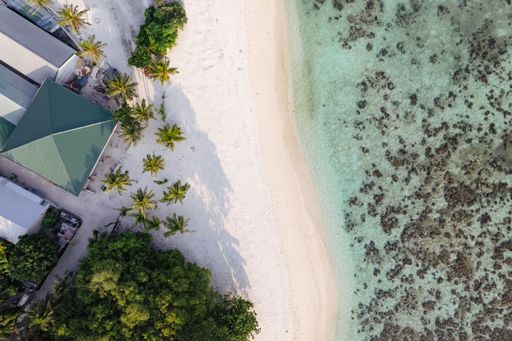 A beautiful bird's eye view of a white beach with bright turquoise tides washing over it in Kamadhoo, Maldives