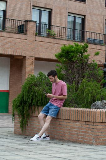 A Hispanic young male sitting checking his phone in the street in Cudillero, Spain