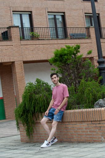 A handsome young Hispanic male sitting on stone fence in the street in Cudillero, Spain