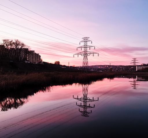 A transmission tower reflecting on a small pond surrounded by buildings during a beautiful sunset
