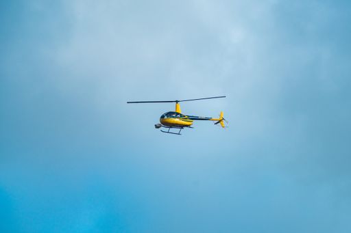 A low angle of a yellow helicopter flying in a blue sky