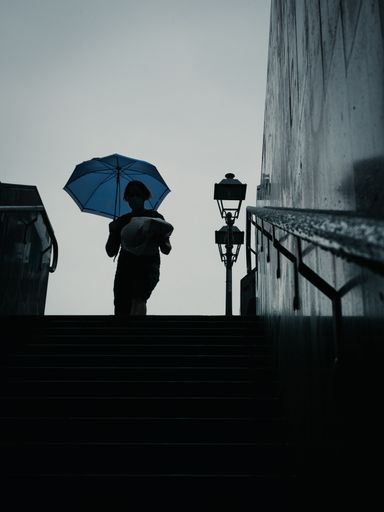 A vertical shot of a person walking down the stairs under the rain