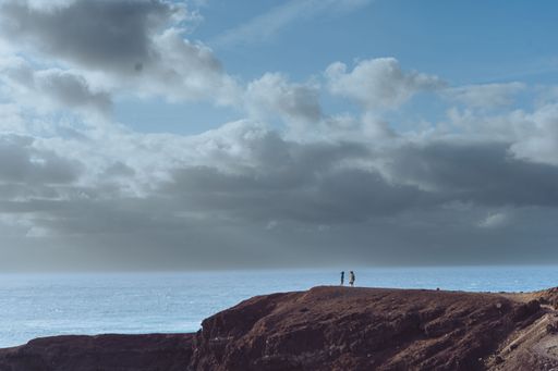 A distant shot of females standing on a cliff against the blue sea on a summer day