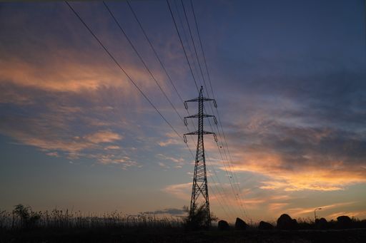 A silhouette of a transmission tower against a sunset sky