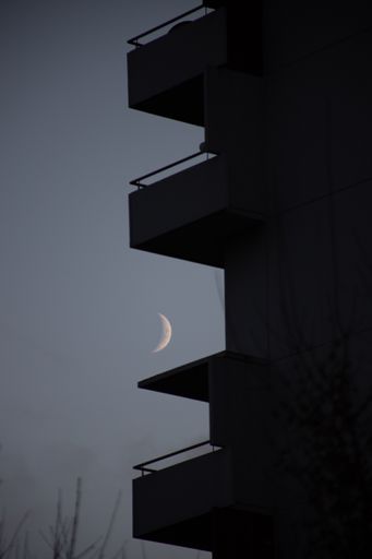 A vertical shot of a building silhouette with balconies in the evening on the moon backgroun