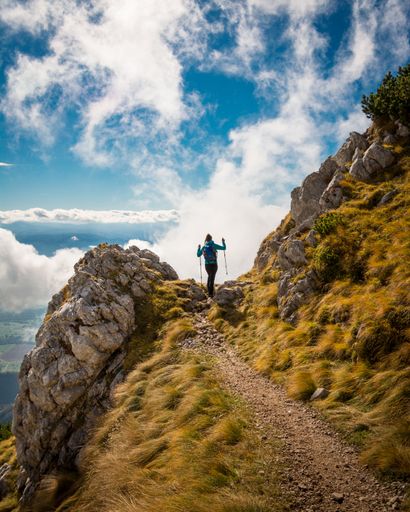 A vertical shot of a hiker going up the rocky mountain with the help of trekking poles