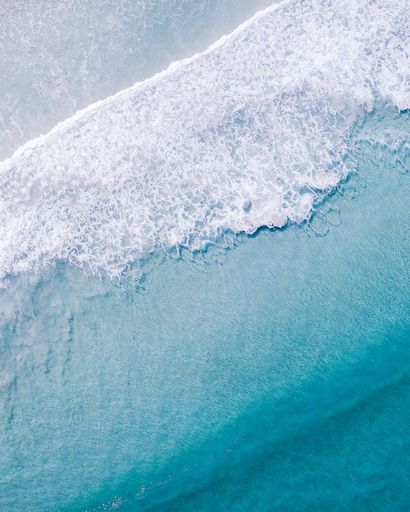 A vertical aerial shot of clear ocean water with foamy waves in Western Australia