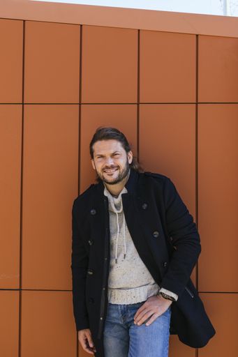 A man leaning against a red wall in winter talking on the phone