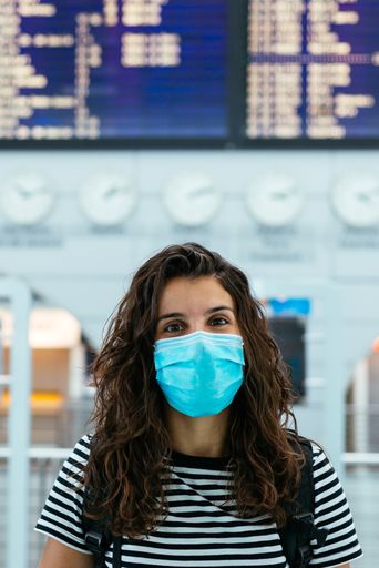 A vertical shot of a Caucasian woman wearing a face mask in the airport during coronavirus pandemics