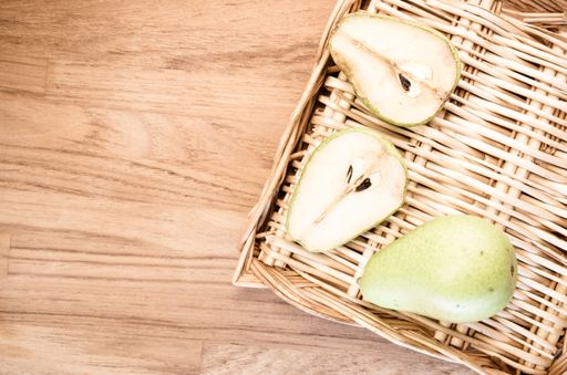 A high angle shot of fresh pears and a basket on a wooden surface