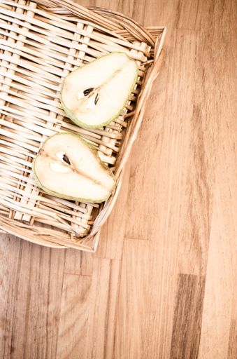 A vertical shot of a half-cut pear on a basket on a wooden surface