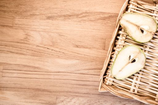 A high angle shot of a half-cut pear on a basket on a wooden surface