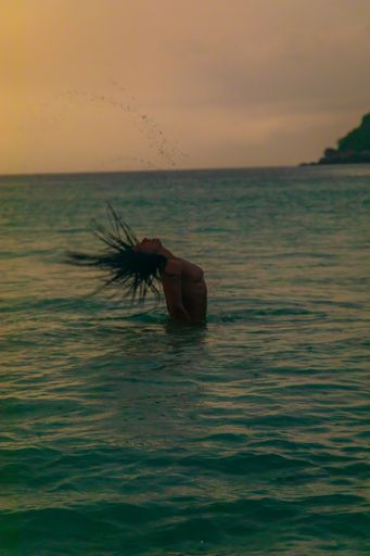 A vertical shot of a female having fun playing with her hair in the ocean at Freedom Beach, Thailand