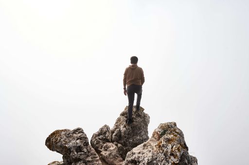 A male hiker on high big rocks against the white sky