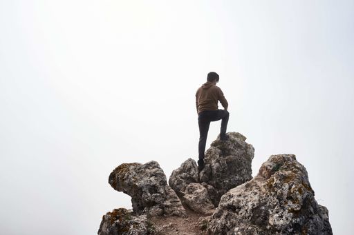 A male hiker on high big rocks against the white sky