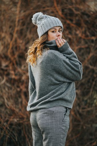 A vertical shot of a young lady wearing a gray turtleneck sweater and a hat