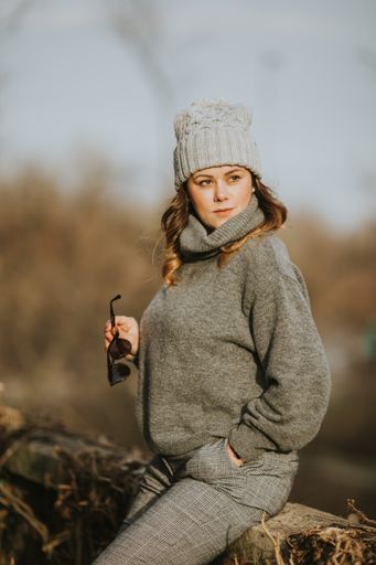 A vertical selective focus shot of a young lady wearing a gray turtleneck sweater, trousers, and a hat