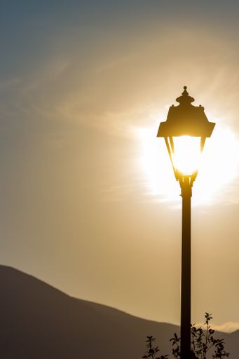 A vertical shot of a street lamp with the sun shining in it