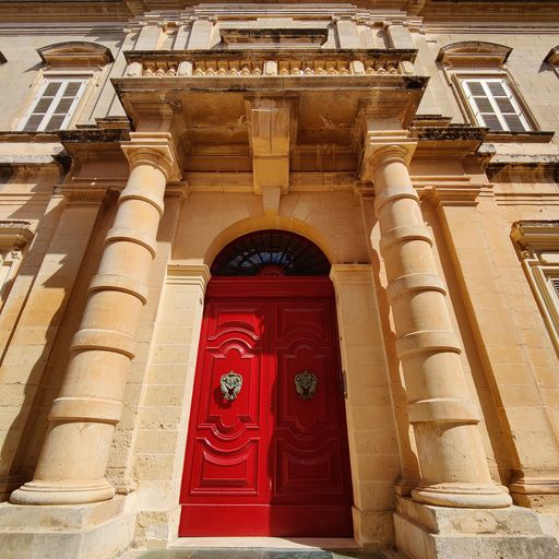 A front facade of an ancient building with a red door in Mdina, Malta