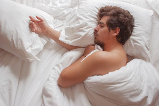 An overhead shot of a young Caucasian male sleeping in his bed at home. He is enjoying his sleep routine on a sunny day.
