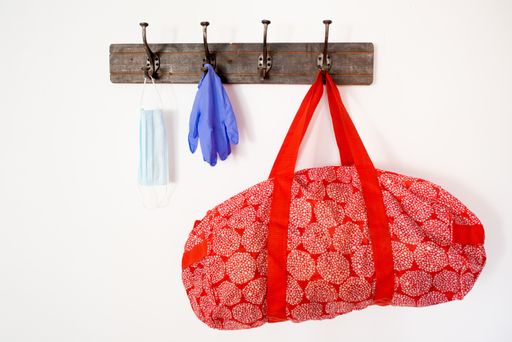 A red bag, medical gloves, and a mask hanging from the hanger on a white wall