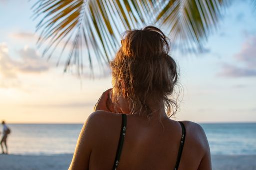A female drinking coffee while looking at the sea shot from behind