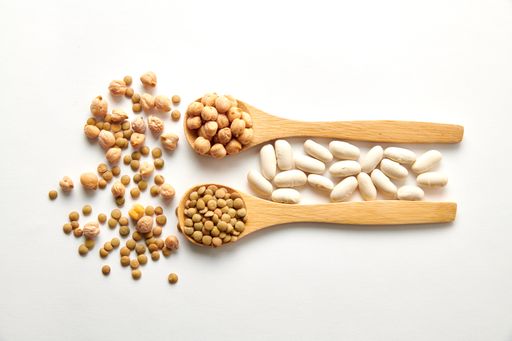 A top view shot of dried lentils, chickpeas, and white beans with wooden spoons on white background