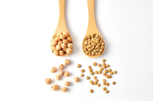 A top view shot of dried lentils, chickpeas with wooden spoons isolated on white background