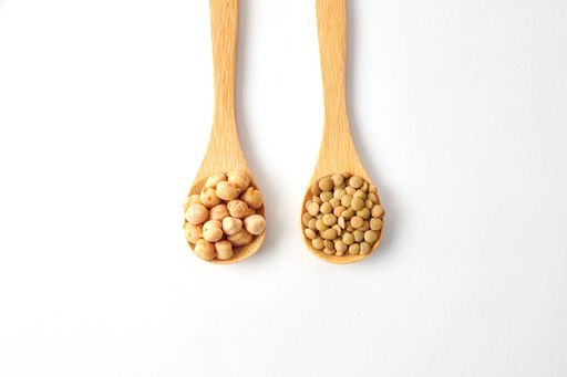 A top view shot of dried lentils, chickpeas with wooden spoons isolated on white background