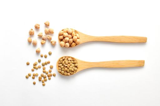A top view shot of dried lentils, chickpeas with wooden spoons isolated on white background
