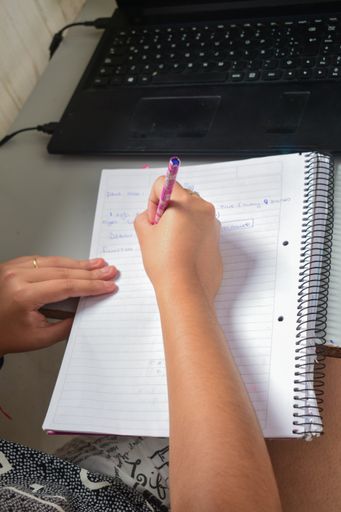 A selective focus shot of female writing some notes in a notebook from a laptop