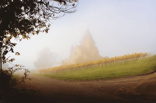 A scenic view of a winding road leading up to a chapel on a foggy day