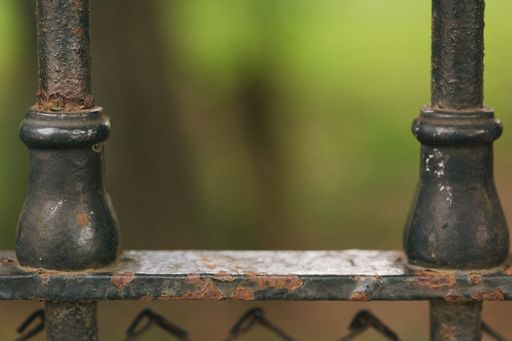 A close-up shot of some rusty metallic fence details in a blurry background.
