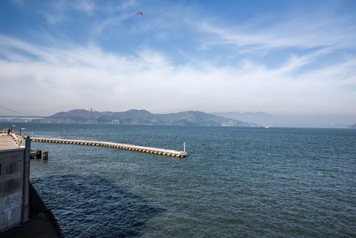 A landscape view of San Francisco Harbor with breakwater and bridge on the horizon with blue sky