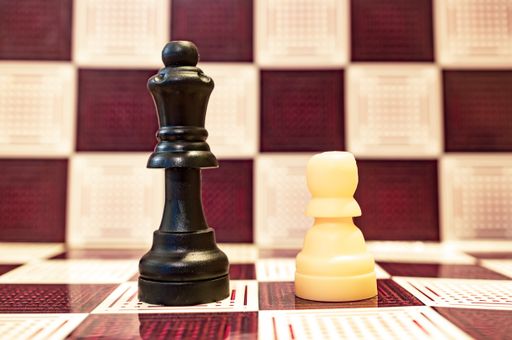 A selective focus closeup of a black queen and white pawn chess pieces on a chessboard