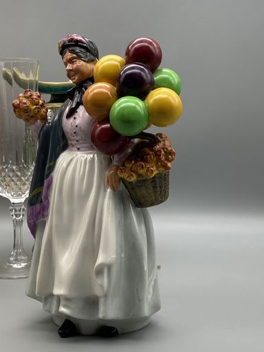 A vertical shot of an old woman porcelain figurine holding balloons