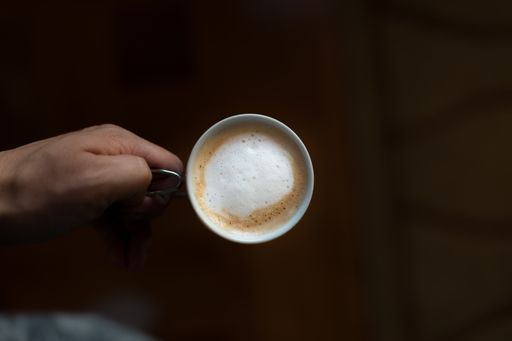 A top view of man's hand holding a Caffe latte in mug against a blurry background