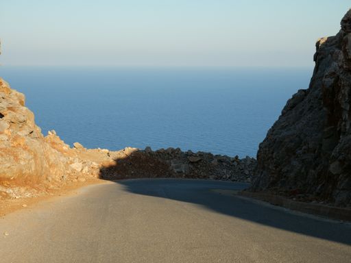 A beautiful view of the road that goes in between the rocky cliff that leads to the ocean