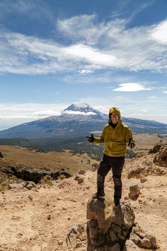 A vertical shot of an adultHispanic male hiker standing on a hill under the sunlight and a blue cloudy sky