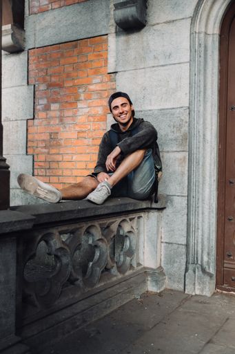 A man sitting at the door of his house with a backpack