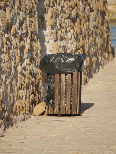 A vertical shot of a wooden trash bin with a black bag