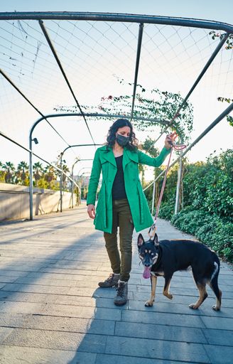 A vertical shot of a young woman wearing green coat walking her dog in the park