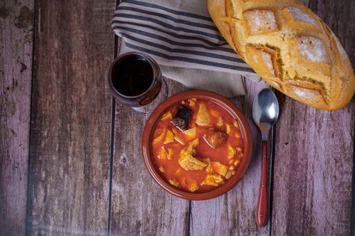clay casserole with Madrid-style stewed tripe, typical spanish food on a wooden table with a brick wall in the background.