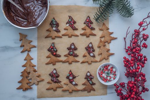 A top view of chocolate cookies in form of Christmas trees, decorated with colorful edible beads