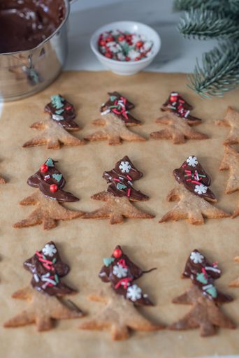 A vertical top view of chocolate cookies in form of Christmas trees,decorated with colorful edible beads