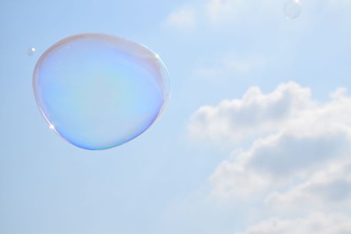 A closeup of a bubble flying in a cloudy blue sky on a sunny day