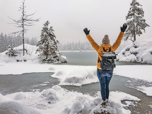 A back view of a young female hiker with a backpack enjoying the view of a frozen lake
