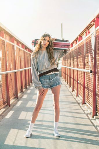 A vertical shot of a Caucasian cool sporty woman wearing shorts and holding a skateboard